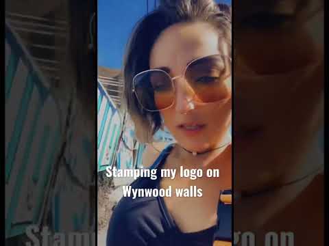 A woman showcases her logo while filming in front of colorful murals at Wynwood Walls, Miami.