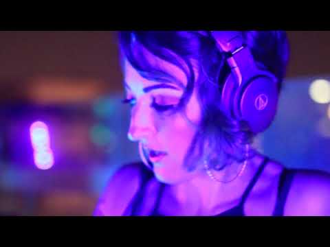 A close-up of a woman with headphones, illuminated by vibrant purple lights while mixing music.